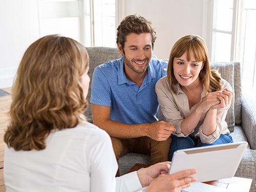 safer home services team member showing service brochure to young adult couple seated on a sofa