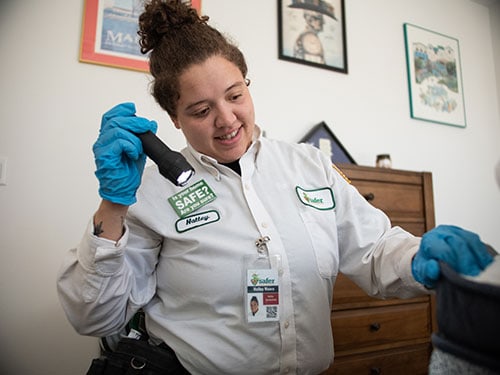 a safer home services employee inspecting a room for infestation with a flashlight